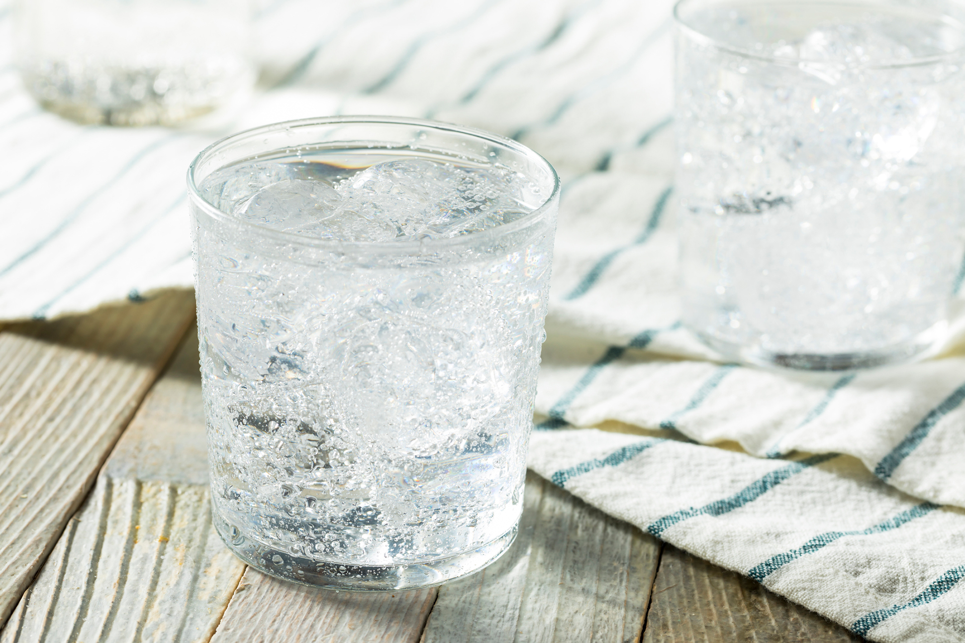 Two glasses of water sitting on a tea towel on a wood surface